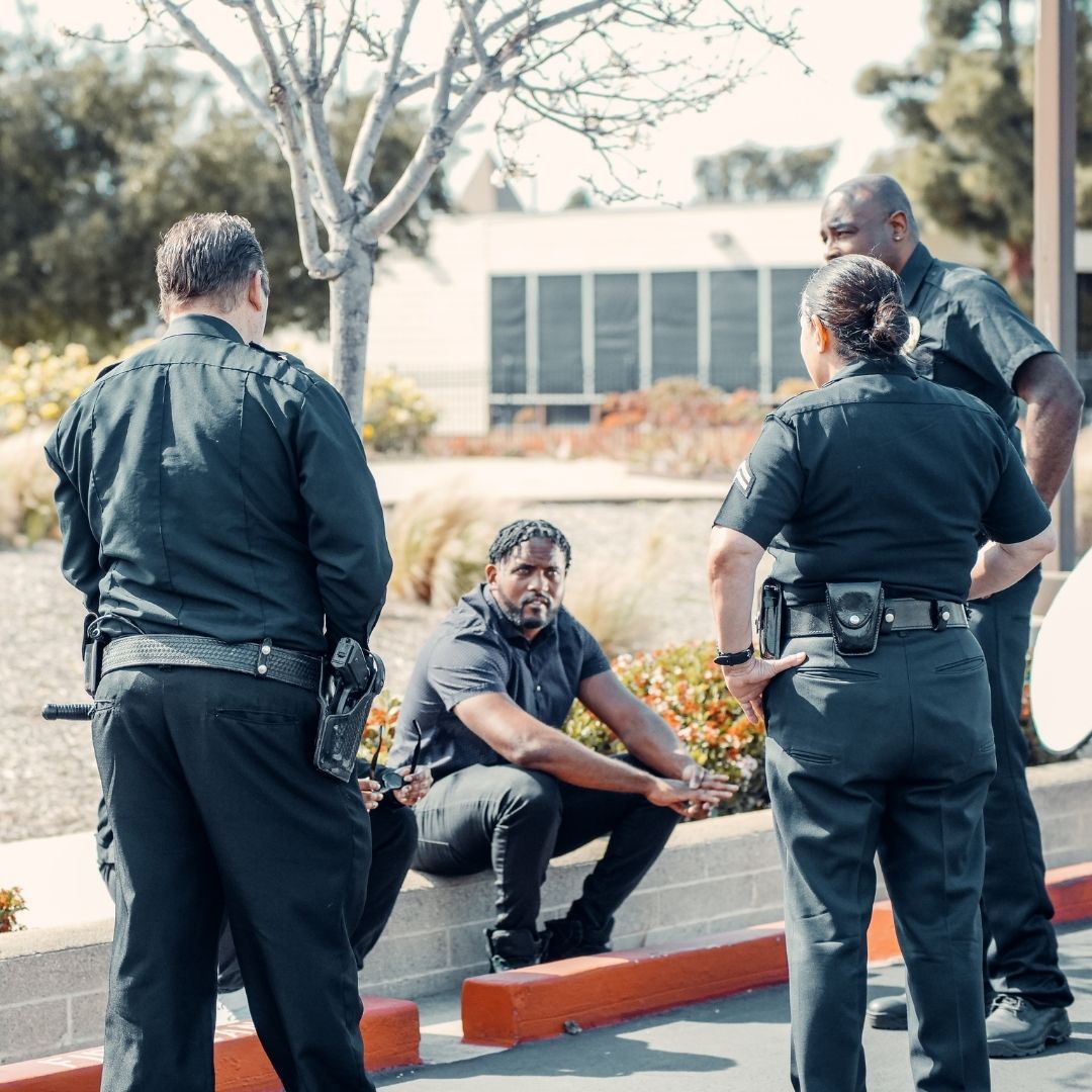 police officers approaching black man sitting on a curb