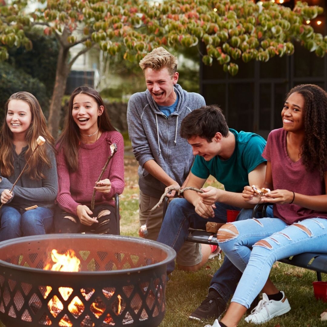 A group of teens around a fire pit laughing